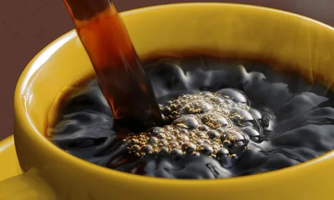 Fresh coffee pours into a wide yellow cup, the surface full of bubbles