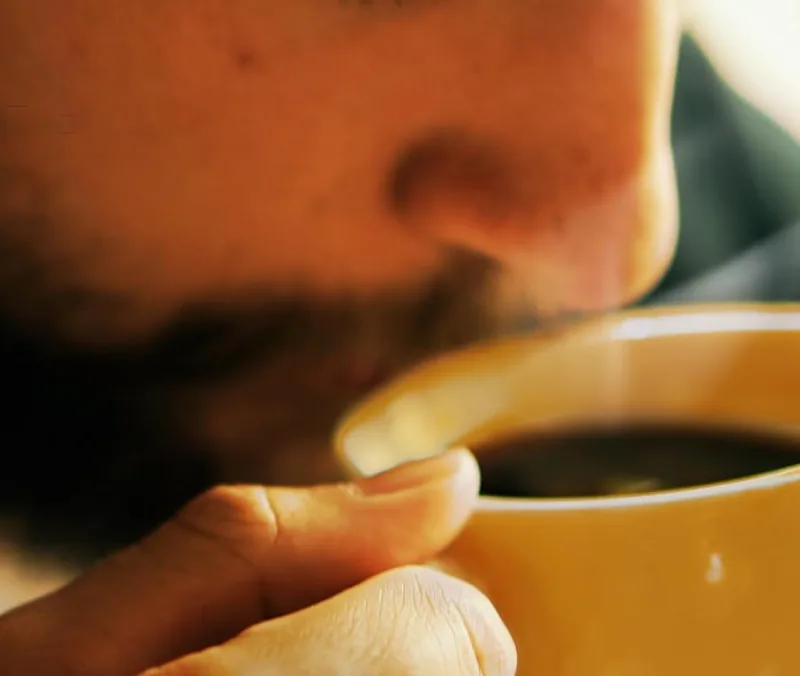 A man holds a yellow cup of coffee close and breathes in the aroma